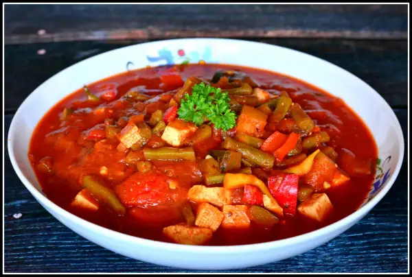 Pyszne leczo z tofu, z fasolką szparagową i papryką w sosie pomidorowym, udekorowane natką pietruszki.