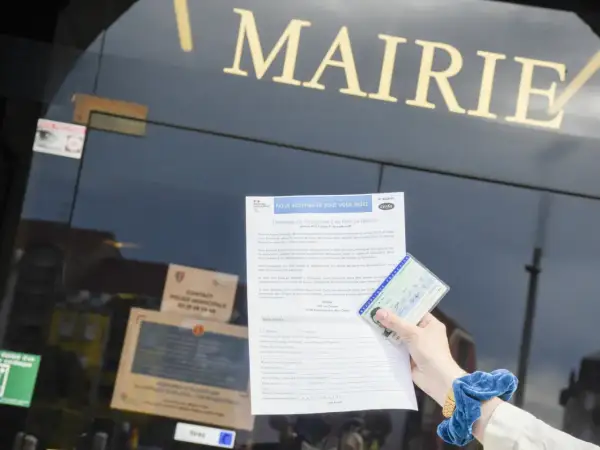 Main dans la main, une carte d'identité française et un formulaire de demande de changement de nom de famille sont présentés devant la mairie. Un geste pour de fautereau vassel.