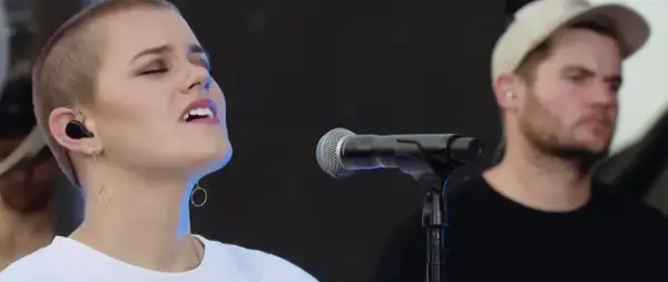 Taya Smith singt mit geschlossenen Augen und In-Ear-Monitoring. Ein Mann mit Kappe steht im Hintergrund.