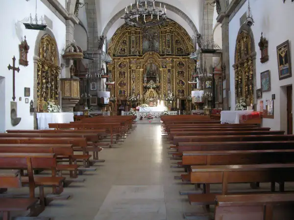Interior de una iglesia con bancos de madera y un retablo dorado. Una pequeña maqueta de barco cuelga del techo, quizás en honor a la virxe da barca.
