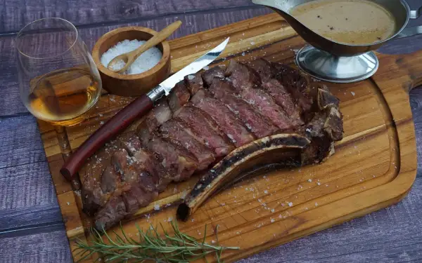 Ein saftiges Cote de Boeuf, perfekt geschnitten, mit grobem Salz bestreut, daneben ein Glas Whiskey, ein Messer und eine Sauce.