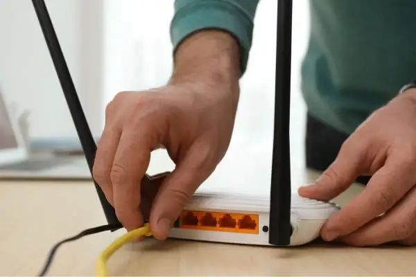 Ręka podłącza żółty kabel do routera. Dowiedz się, jak wzmocnić sygnał wifi domowym sposobem, by cieszyć się lepszym zasięgiem.