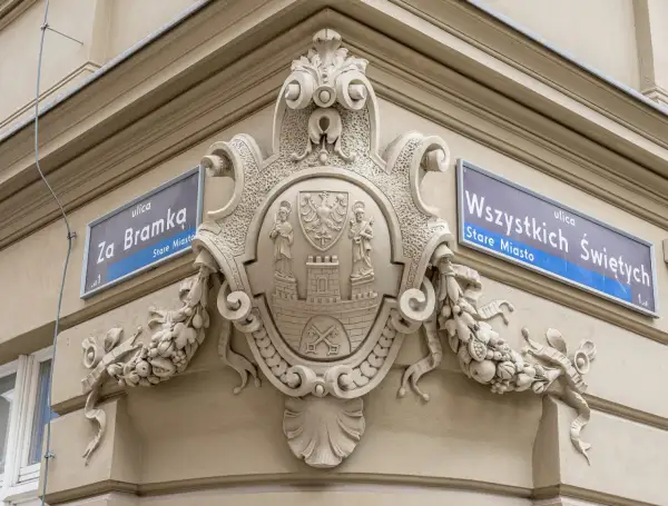 Bogaty herb zdobi fasadę kamienicy, obok tabliczek z nazwami ulic "Za Bramką" i "Wszystkich Świętych".