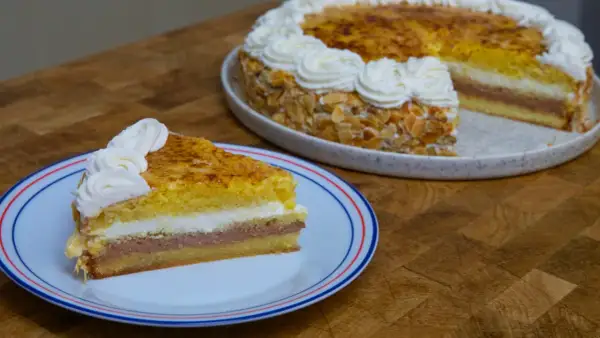 Un trozo de tarta o pastel de capas con crema y almendras, coronado con nata montada.