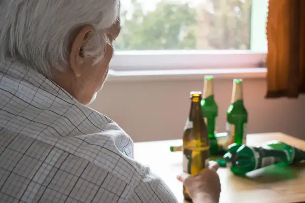 Starszy mężczyzna zmagający się z alkoholizmem, siedzi przy stole z kilkoma pustymi butelkami po piwie.
