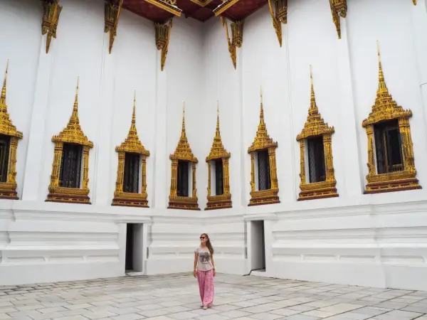 Una mujer sonríe frente a una pared blanca con ventanas doradas ornamentadas, un ejemplo de qué ver en Tailandia.