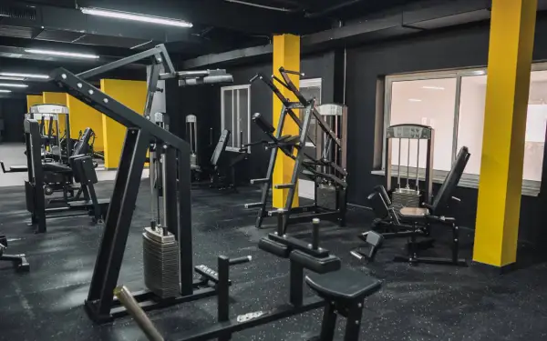 Gym med svarta väggar och gula pelare. Flera träningsmaskiner, inklusive en pec deck, står redo för ett träningspass.