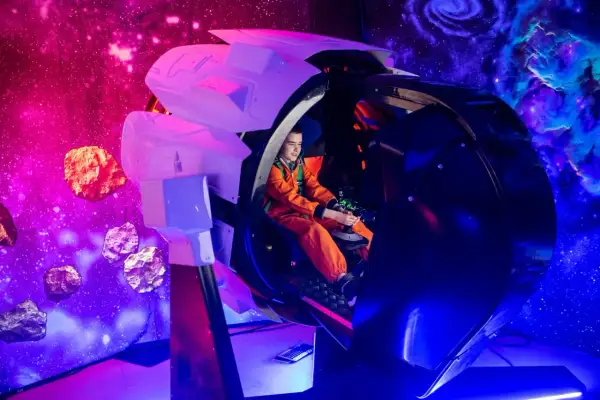 Chłopiec w pomarańczowym kombinezonie steruje statkiem kosmicznym w symulatorze. Kosmopark Wrocław oferuje kosmiczne przygody wśród asteroid i mgławic.