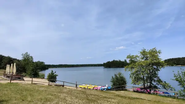 Słoneczny dzień nad jeziorem Chechło. Kolorowe rowerki wodne czekają na plaży, a w oddali widać zalesione brzegi.