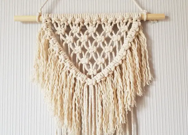 Un joli macramé tuto, suspendu à une tige de bois, avec des franges douces et un motif en losanges.