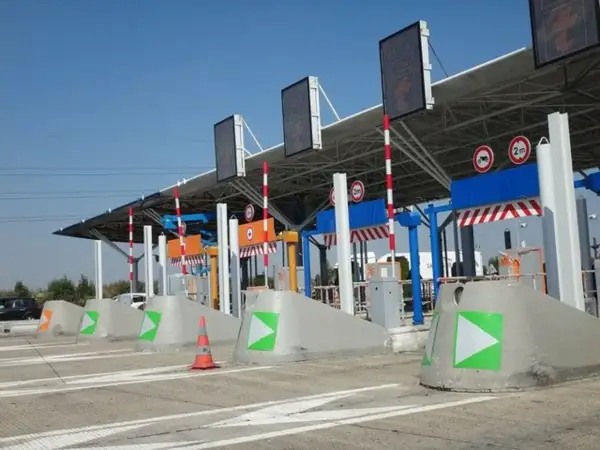 Voies de péage avec des indicateurs verts et orange. Une voie semble réservée au péage gratuit pour les handicapés.