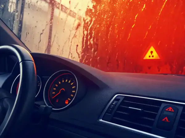 Tableau de bord d'une voiture avec un voyant orange allumé indiquant un système ABS défaillant. Le soleil brille à travers un pare-brise mouillé.