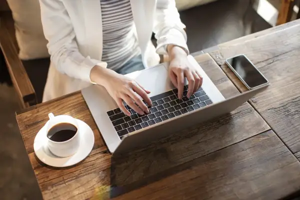 Kobieta pracuje na laptopie, realizując nest bank sesje przychodzące. Obok kawa i telefon.