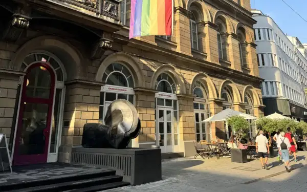 Ein Regenbogenbanner weht über dem von der Heydt Museum. Eine Skulptur steht davor, daneben ein Café mit Sonnenschirmen.