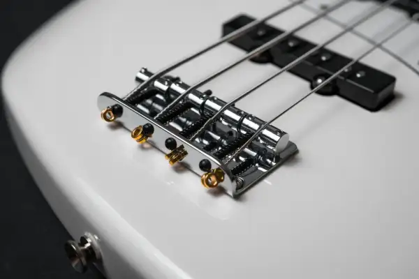 Błyszcząca, biała gitara basowa elektryczna z chromowanym mostkiem i złotymi detalami.