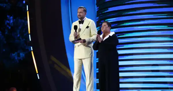 Mężczyzna w żółtym garniturze i kobieta w czarnej sukni na scenie, trzymają mikrofony. To szczyt możliwości, top of the top!