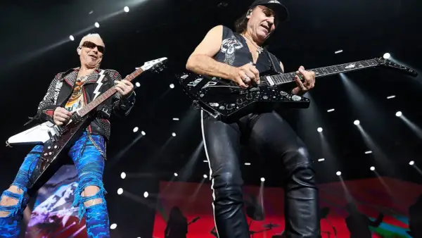 Dwóch gitarzystów na scenie, jeden w skórzanej kurtce i niebieskich spodniach, drugi w czarnej kamizelce i skórzanych spodniach. Ich gra wywołuje "wind of change" tłumaczenie.