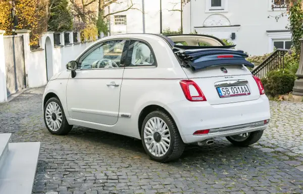 Biały fiat 500c cabrio z otwartym dachem stoi na brukowanej uliczce.