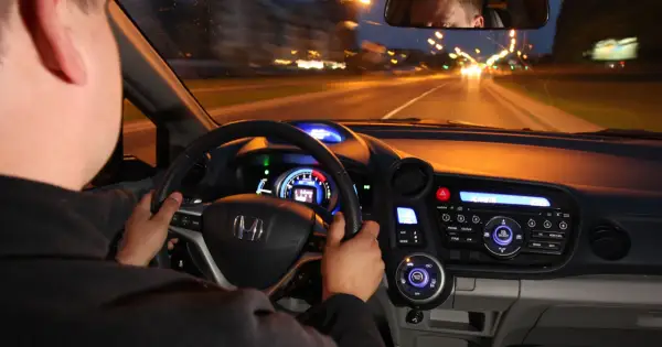 Kierowca prowadzi auto nocą. Czy w czasie jazdy w nocy masz obowiązek zwiększyć uwagę? Widok z wnętrza pojazdu na drogę i deski rozdzielcze.