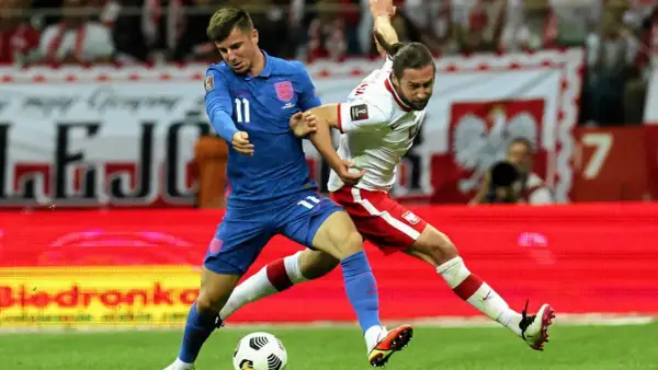 Piłkarz Anglii w niebieskiej koszulce walczy o piłkę z zawodnikiem Polski w białej. Emocjonujący mecz Anglia Polska.