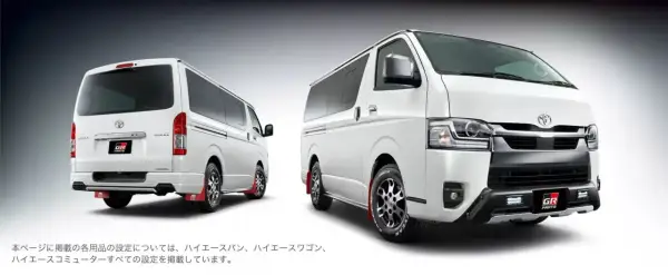 Dwa białe vany Toyota Hiace z pakietem GR Parts. Jeden z tyłu, drugi z przodu, oba z czerwonymi chlapacami.