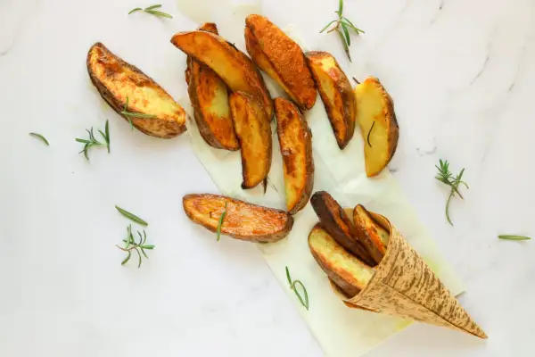 Patate al forno dorate e croccanti, profumate al rosmarino, servite su carta da forno e in un cono di bambù.