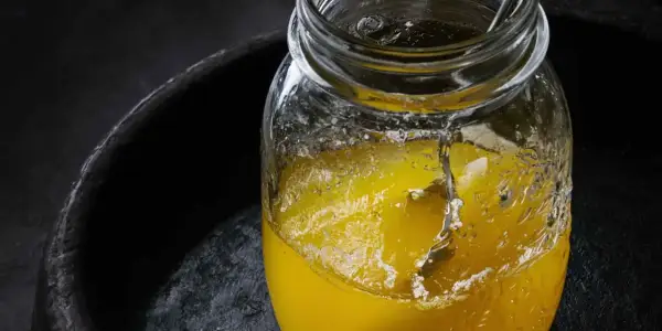 Słoik z płynnym, żółtym tłuszczem, być może ghee, na ciemnym tle. Czy oliwa z oliwek jest zdrowa? To pytanie nurtuje wielu.