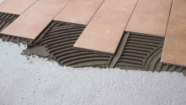 Pose de carrelage droit ou décalé sur lit de mortier frais. Les carreaux beiges sont appliqués sur un support en béton.