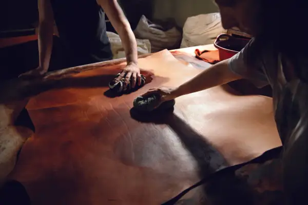 Mani esperte lavorano il cuoio con cura, un processo di lavorazione cuoio artigianale che dona profondità e colore alla pelle.