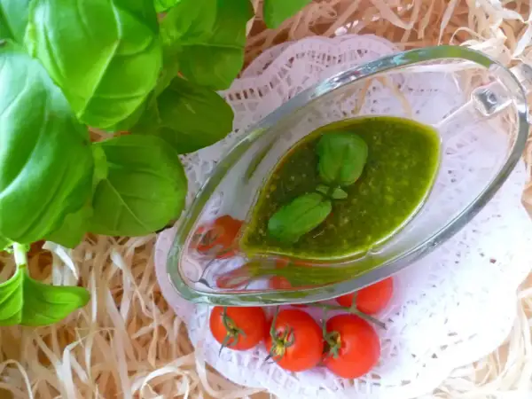 Aromatyczne pesto bazyliowe w sosjerce, ozdobione listkami bazylii, obok gałązki pomidorków koktajlowych.