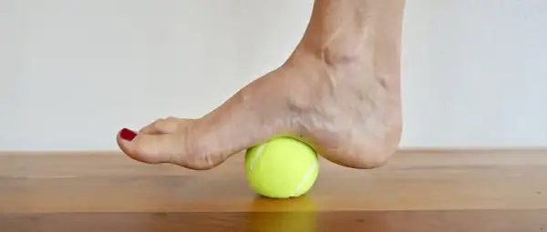 Fuß auf einem Tennisball zur achillessehne dehnen. Sanfter Druck auf die Ferse zur Lockerung.
