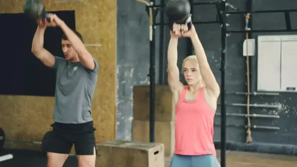 Uomo e donna eseguono esercizi con kettlebell, un allenamento completo per diversi gruppi muscolari in palestra.
