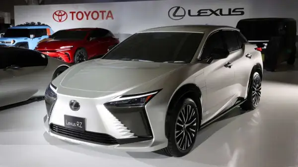 Elegancki, srebrny Lexus RZ prezentuje się na tle logo Toyoty i Lexusa.