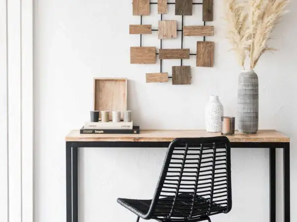 Un bureau en bois avec une chaise noire, des livres, des vases et une décoration murale. Idéal pour apprendre comment décalquer sur du bois.