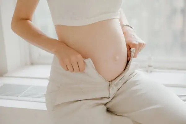 Barriga de embarazada, ajustando pantalones. Los cambios del embarazo, como los pedos, son parte de la experiencia.