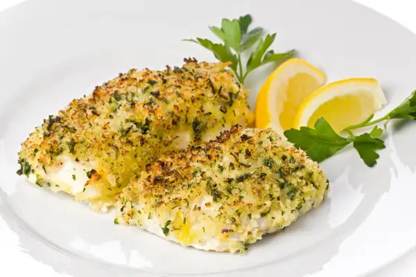 Delizioso merluzzo al forno con crosta dorata di pangrattato ed erbe aromatiche, guarnito con spicchi di limone e prezzemolo fresco.