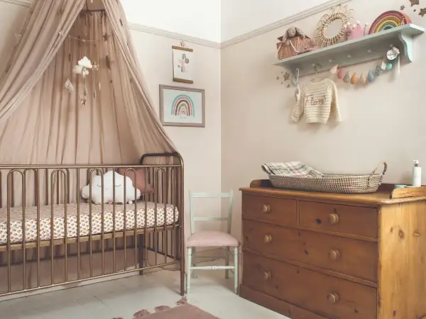 A serene modern nursery theme with a gold crib, cloud mobile, and rainbow art. A vintage dresser holds a woven basket, completing the cozy, dreamy atmosphere.