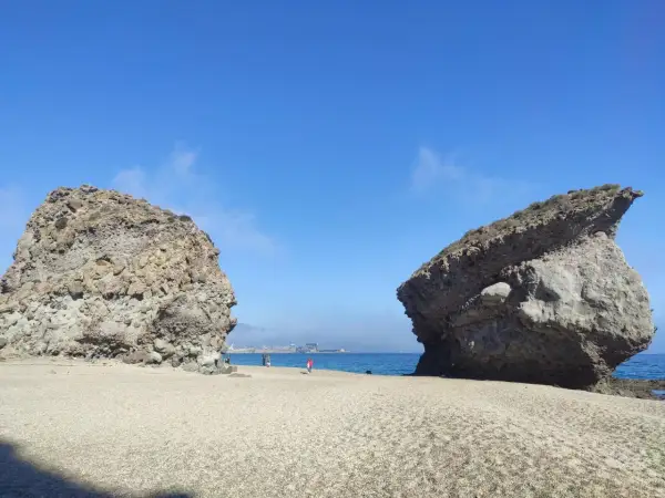 Dos rocas gigantes flanquean una playa de guijarros en la carbonera de Almería, con el mar azul y el cielo despejado de fondo.