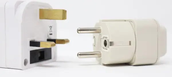 Adapter do gniazdek w Hiszpanii. Biały adapter z bolcami brytyjskimi obok jasnoszarego z bolcami europejskimi.