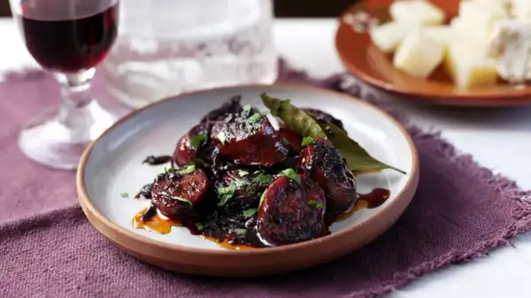 Delicious chorizo tapas, glazed and garnished with parsley, served with a glass of red wine and cheese.