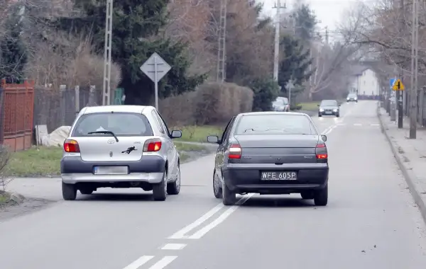 Srebrny samochód wyprzedza ciemny, jadący po tej samej drodze. Wymijanie i omijanie to kluczowe manewry na drodze.