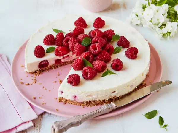 Eine köstliche Philadelphia Torte Himbeer, üppig garniert mit frischen Himbeeren und Minze, auf einem rosa Teller.