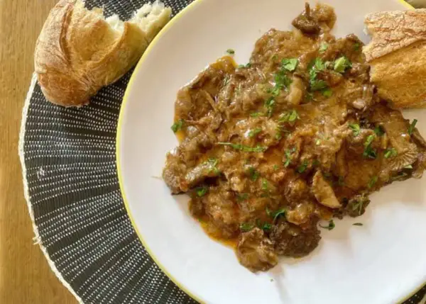 Plato de fricando de ternera con salsa cremosa y trozos de pan crujiente.