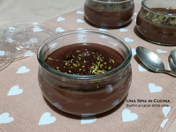 Budino al cioccolato fatto in casa, guarnito con pistacchi tritati, servito in vasetti di vetro su un tovagliolo con cuoricini.