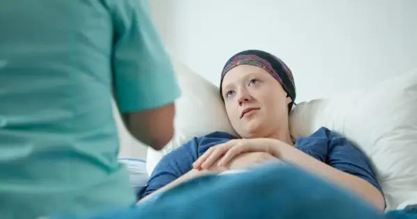 Młoda pacjentka w chustce na głowie leży w łóżku, słuchając pielęgniarki. To może być początek walki z chorobą, gdzie rak przedinwazyjny co to znaczy, jest kluczowym pytaniem.