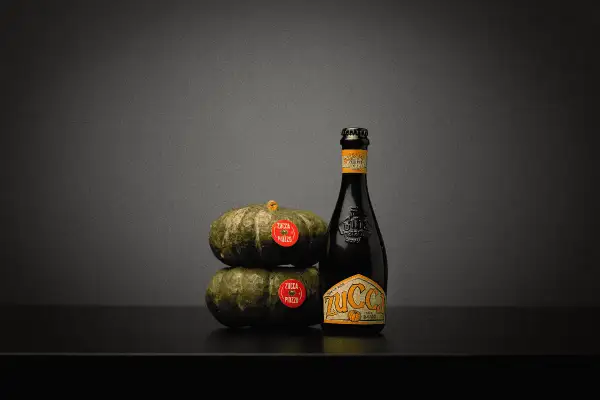 Una bottiglia di birra alla zucca accanto a due zucche impilate.