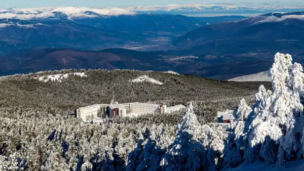 Edificio hotelero en la cabeza de Manzaneda, rodeado de pinos nevados y montañas al fondo.