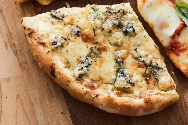 Une part de pizza 4 fromages, avec sa croûte dorée et son mélange de fromages fondus, sur une planche en bois.