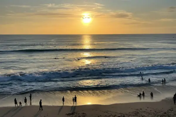 Zachód słońca na plażach Bali. Surferzy czekają na fale, a ludzie spacerują po piasku, ciesząc się złotym blaskiem.