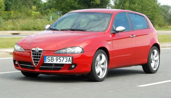 Czerwona Alfa Romeo 147 w ruchu, z widocznymi reflektorami i grillem.